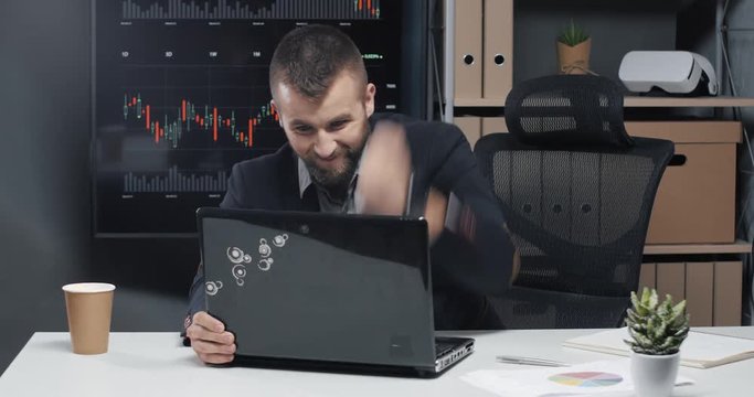 Young man in a modern office works at the computer, hits the screen and destroys the laptop, aggressive emotions.