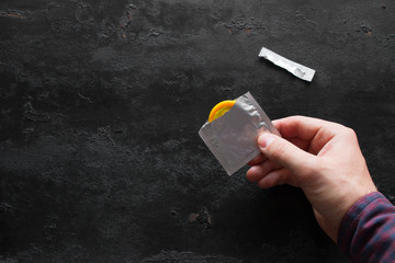 hand holds yellow condom on black background with place for text