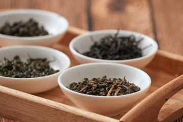 the white drinking bowls of assortment of dry tea in order on wooden background