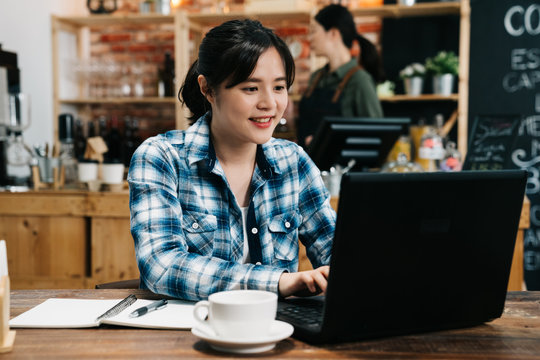 Image of happy asian young woman using laptop computer while sitting at cafe bar. japanese girl sitting in coffee shop and working on notebook pc. female barista in counter making cooking indoors.