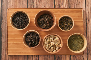 assortment of dry tea in white bowls on wooden surface