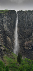 high waterfall plummets off a rock and grass cliff in the Swiss Alps