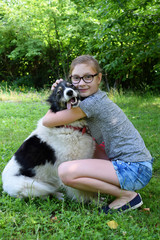 Naklejka na ściany i meble Girl playing with dog on grass. Teenager hugging Carpathian Shepherd Dog in the summer park. Friendship concept of man and animal