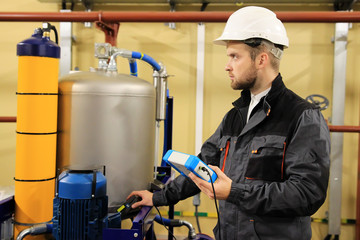 HVAC maintenance engineer checking technical data of heating system equipment in boiler room
