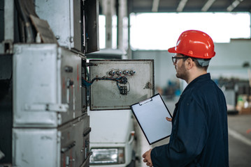 Electrician looking at electric cabinet at large factory hall.