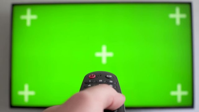 Flat screen TV with green screen composited Male hand holding the TV remote control Channel surfing. focused on the hand and remote control.