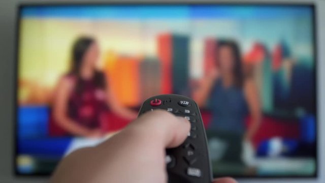Channel surfing television news channels, focused on the hand and remote control. Internet Connected TV. Male hand holding the TV remote control
