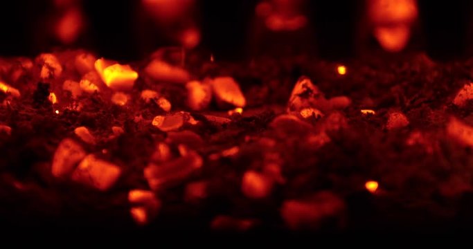 Red hot coals glow beneath a fire as more coals fall down. Macro shot