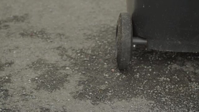 Close up of person pushing garbage bin on wheels