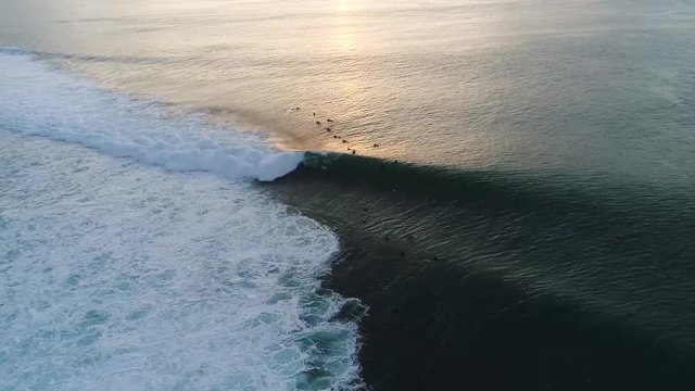 Aerial shot of surfers out on the ocean catching waves at Padang Padang Beach in Bali, Indonesia, at sunset