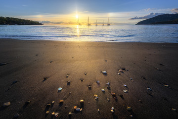 Wide angle lens shot of black sand beach at sunset with boats in the far side, Vulcano Island,...