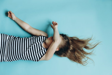 Girl laying on blue background covering face. Child sleeping flat lay top view. Having rest, relaxing. Childhood memories. Beautiful flowing hair. Simple minimalist background, wallpaper