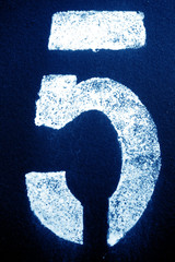 Number 5 in stencil on metal wall in navy blue tone.