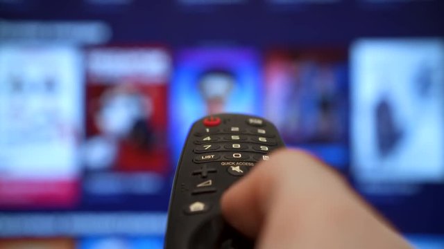 Internet Connected TV hand holding the TV remote control Channel surfing. smart tv. focused on the hand and remote control