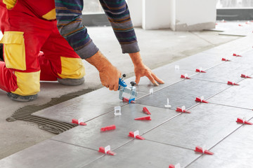 Ceramic Tiles. Tiler placing ceramic wall tile in position over adhesive with lash tile leveling...