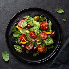 Fresh vegetable salad with tomato, cucumber, bel pepper and olives salad on black plate