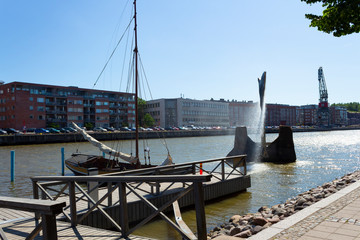 City fountain on the river Auraioki on the embankment of the city of Turku Abo, an old pleasure boat, an old wooden pier and a view of the city in Finland on a sunny summer day.