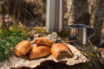 Fresh homemade meat patty cakes, thermos bottle and steel cup on stump in the forest. Picnic. Close up