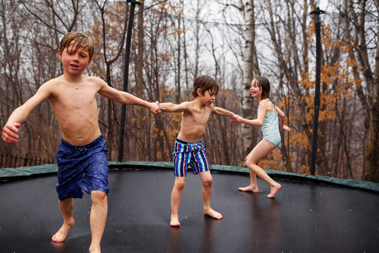 Three children jumping on a trampoline in the rain