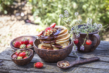 pancakes with chocolate and fresh strawberries in a rustic style on a wooden background