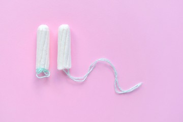 Two cotton tampons for women monthly menstruation with selective focus on blurred pink background. Soft white tampon for female period days on neutral backdrop with empty space for text. Healthcare 