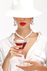 Beautiful girl with a glass of red wine in her hand in an elegant white hat, sunglasses and exquisite jewelry.