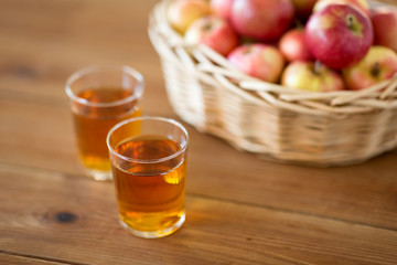 fruits, food and harvest concept - apples in wicker basket and glasses of juice on wooden table