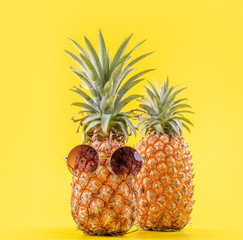 Creative pineapples with sunglasses isolated on yellow background, summer vacation beach idea...