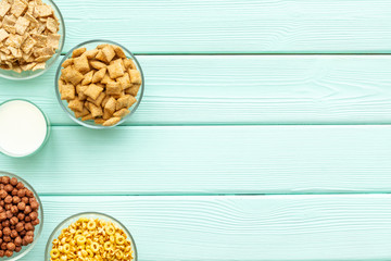 cereals, oatflakes and cornflakes with milk for healthy breakfast on mint wooden background top view mock up