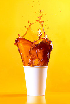 paper cup with coffe splashing in front of orange background