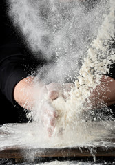 chef in black uniform sprinkles white wheat flour in different directions