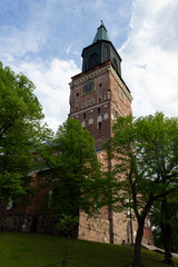 Naklejka premium The tall tower of the historic medieval Gothic Cathedral of the 13th century and the park around Turku Abo on a summer day in Finland. Bottom view of the historic Lutheran Cathedral in Turku.