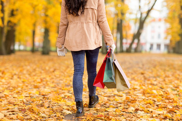 sale, consumerism, season and people concept - woman with shopping bags walking along autumn park