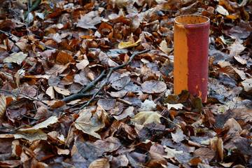 Painted in red and orange colors metal pipe among fall leaves covered ground after rain. Wet autumn leaf textures. Brown and yellow foliage background. Rainy seasonal backdrop. 