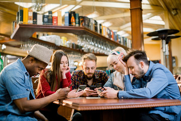 People Meeting Communication Technology Digital Tablet Concept. Group of five multiethnical students sitting in a cafe bar looking at smartphones - Young cheerful friends having fun