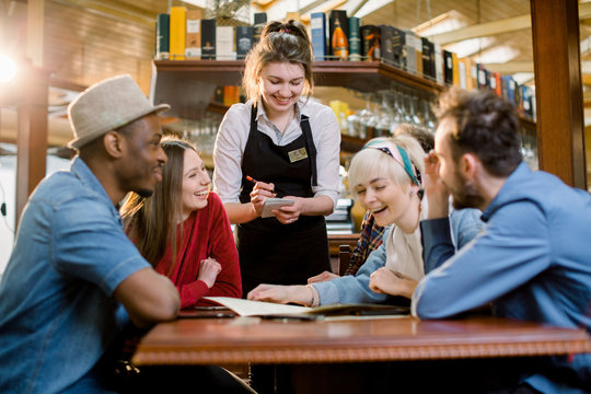 Waitress female welcoming diverse cafeteria pub guests making order waiting staff writing wishes on notepad. Good service dining time, friends meets in public place concept