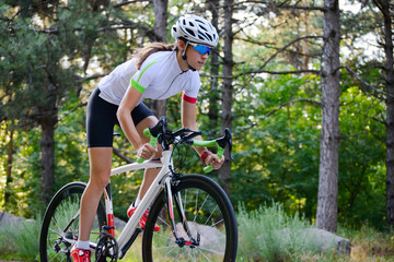 Fototapeta na wymiar Young Woman Cyclist Riding Road Bicycle on the Free Road in the Forest at Hot Summer Day. Healthy Lifestyle Concept.