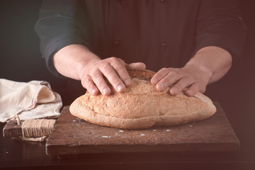 male hands are holding brown baked rye bread over wooden board