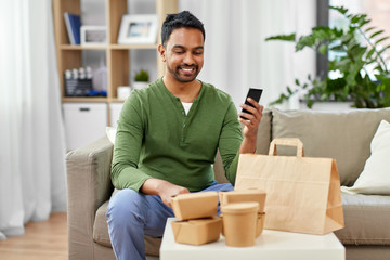 technology, consumption and people concept - smiling indian man using smartphone for food delivery at home
