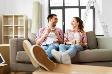 moving, people, repair and real estate concept - happy couple sitting on sofa and drinking coffee...