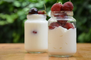 Healthy breakfast - granola, strawberries, cherry, honeysuckle berry, nuts and yogurt in a bowl. Vegetarian concept food. Top view. pudding or cocktail on the background of green foliage