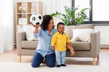 childhood, kids and people concept - happy african american mother and her baby son playing with soccer ball together on sofa at home