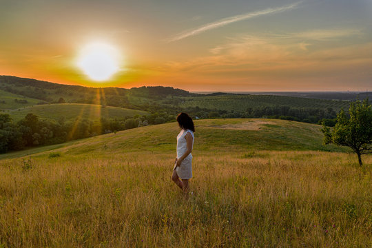 Cute brunette young woman on the summer green hills landscape