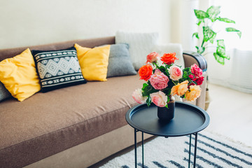 Interior of living room decorated with flowers on coffee table and cozy couch with cushions. Fresh roses