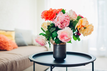 Interior of living room decorated with flowers on coffee table and cozy couch with cushions. Fresh roses