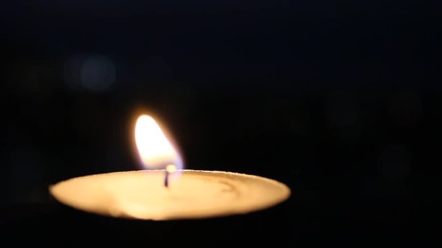 Burning candle in the dark, candlelight with black background, glowing tealight candle