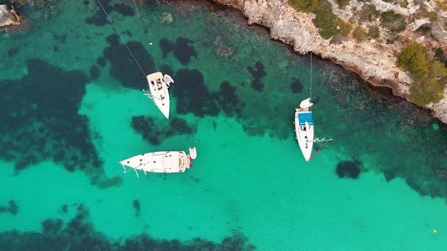 aerial view of three moored sailing boats in clear Mediterranean sea and coral reefs on seafloor, aerial drone rotating high angle shot