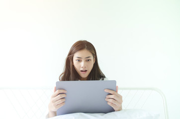 Beautiful Asian woman is smiling.Lady work with laptops on the sofa in the room in the morning.She is happy to get a new job, success, or get good news.In the white room there is a woman inside.