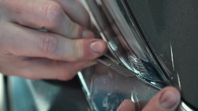 Close up. Applying a protective film on the car headlights. Hand cut with a knife. PPF