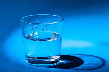 A glass with water drops  on a dark blue background close up